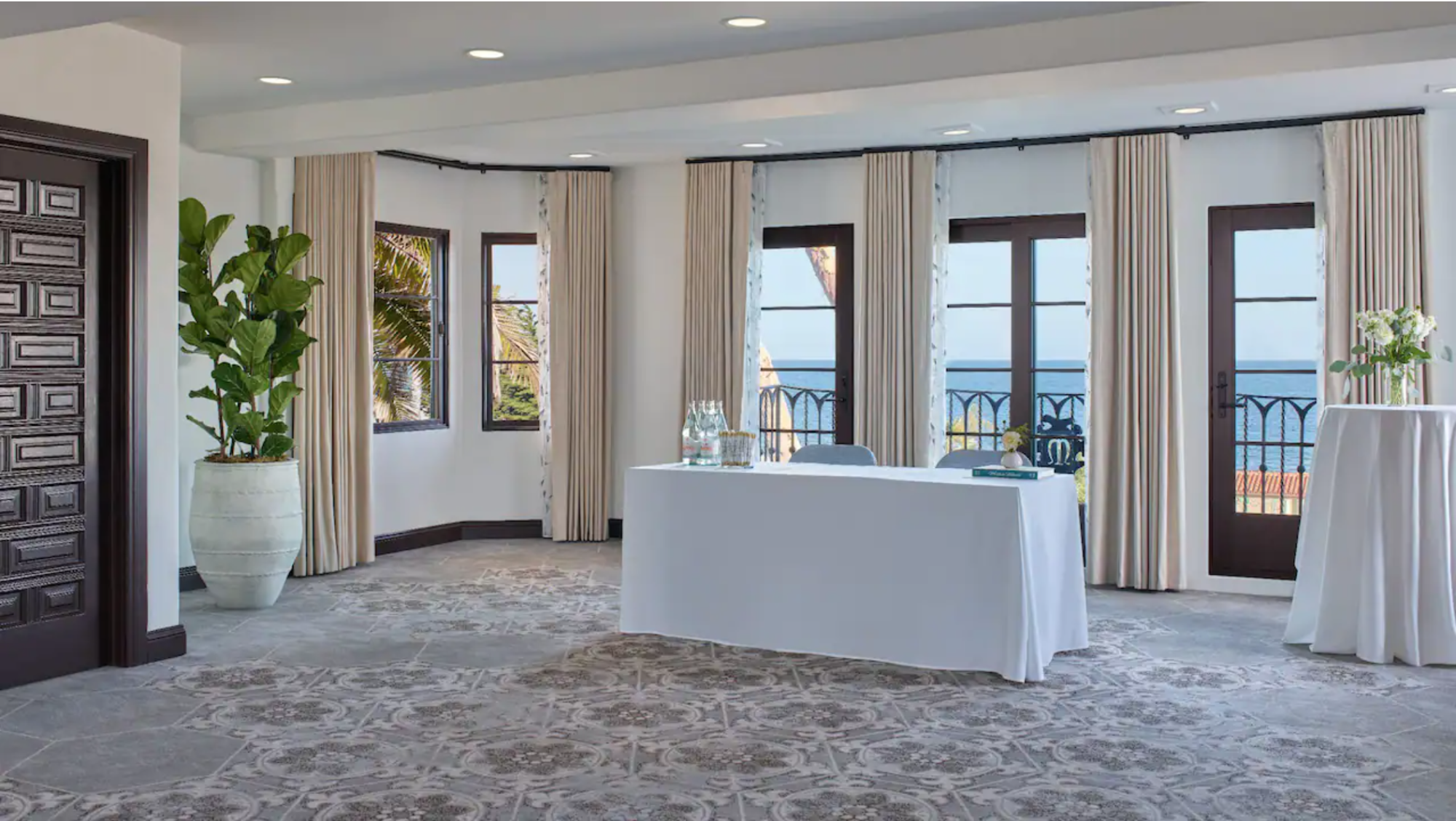 Tables with white linens and drinking glasses and floral centerpieces in front of porch overlooking ocean at Mar Monte Hotel in Santa Barbara, CA