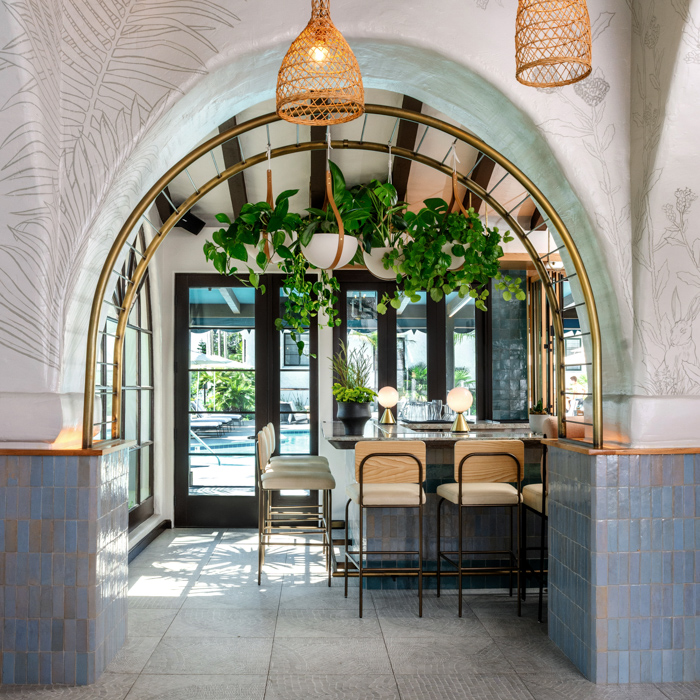 Arch way with potted plants hanging from ceiling near bar area with white chairs at Mar Monte Hotel in Santa Barbara, CA