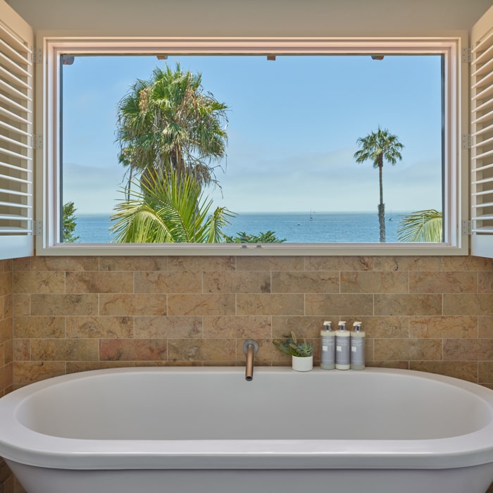 Window over white bathtub showing the ocean and a blue sky and palm trees at Mar Monte Hotel in Santa Barbara, CA