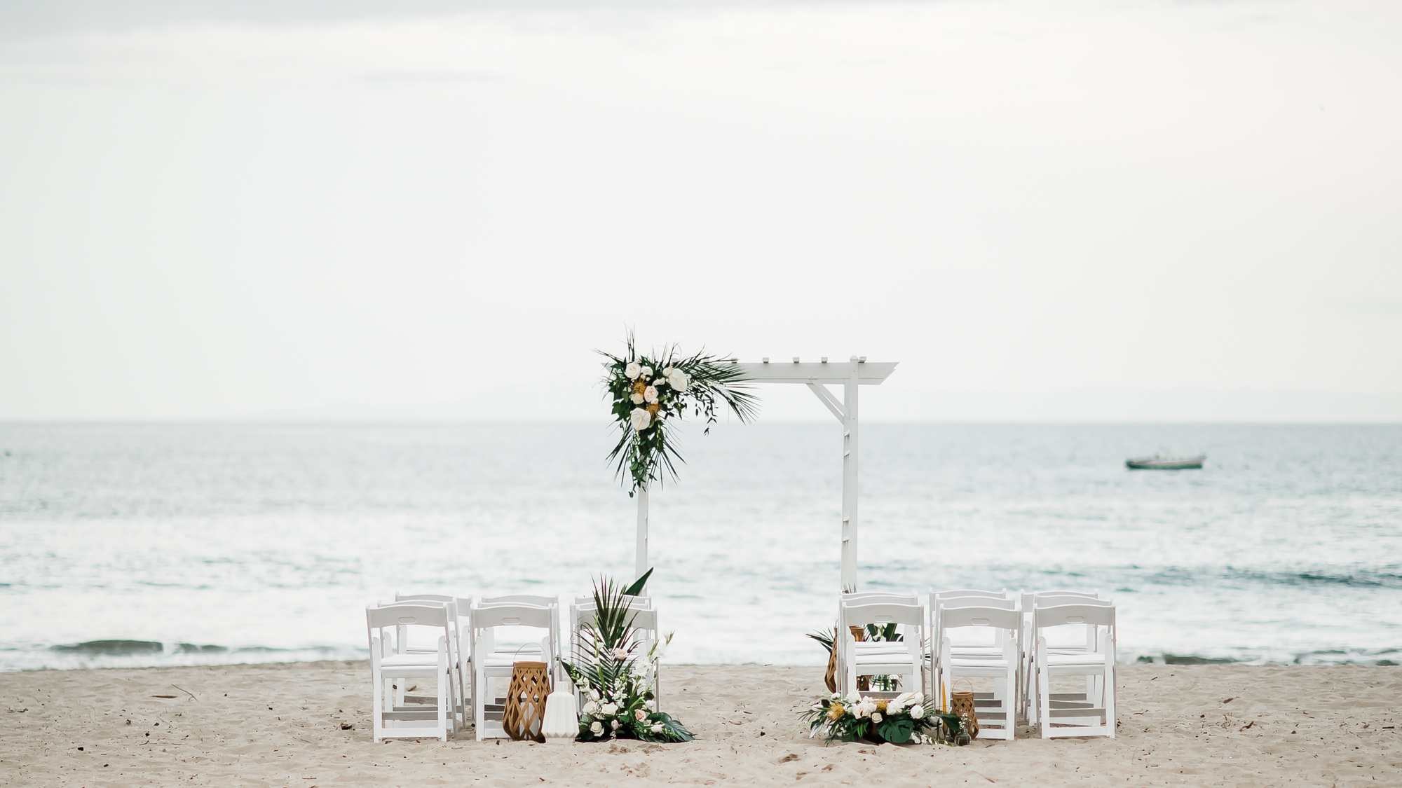 Beach wedding with white chairs and a white archway adorned with white flowers at Mar Monte Hotel in Santa Barbara, CA