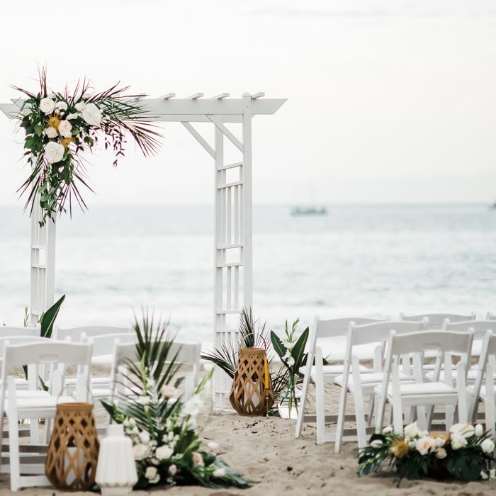 Beach wedding with white chairs and a white archway adorned with flowers at Mar Monte Hotel in Santa Barbara, CA