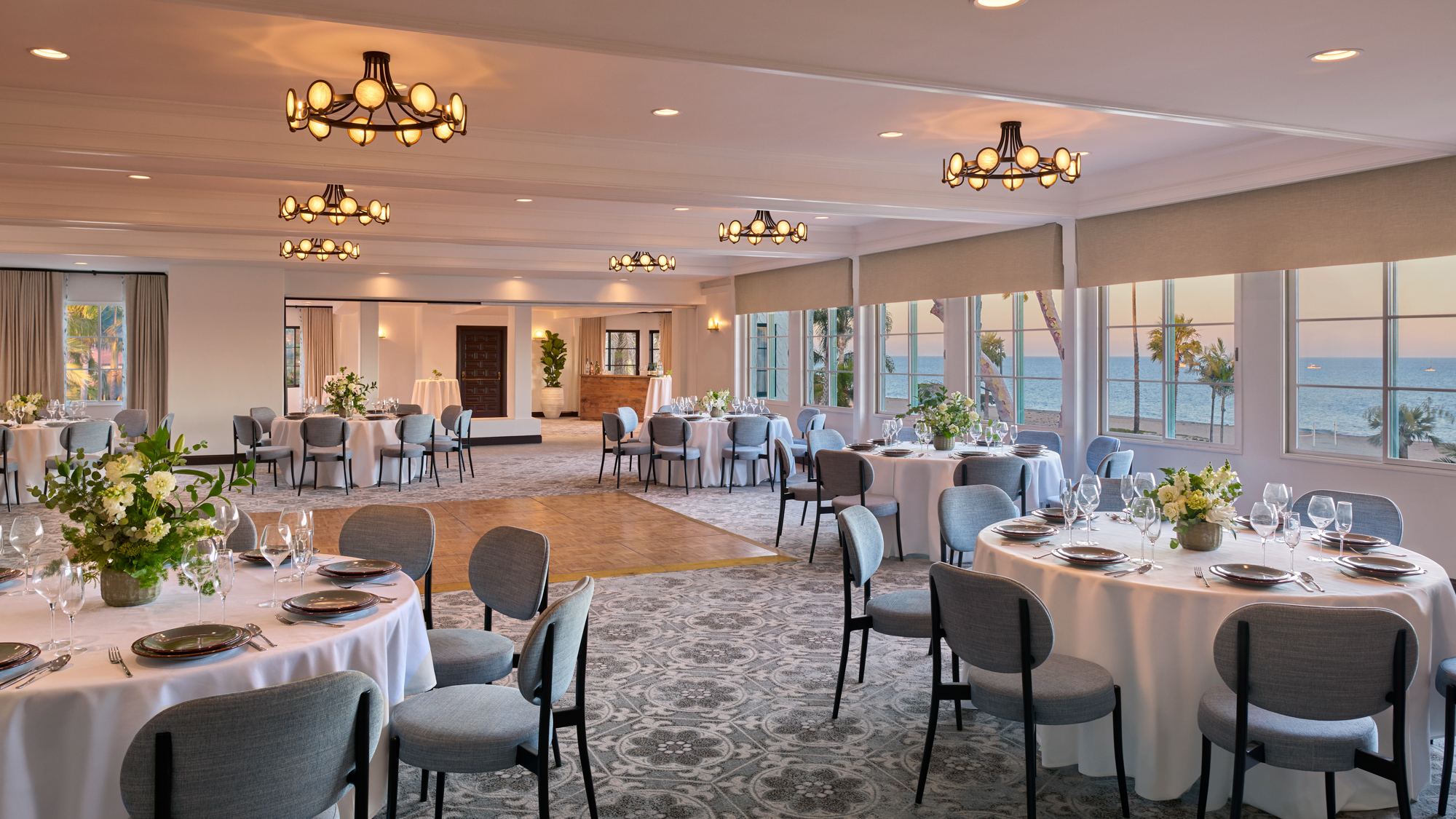 Large event room with blue chairs and round tables adorned with white linens, silverware and glassware as well as flower centerpieces at Mar Monte Hotel in Santa Barbara, CA