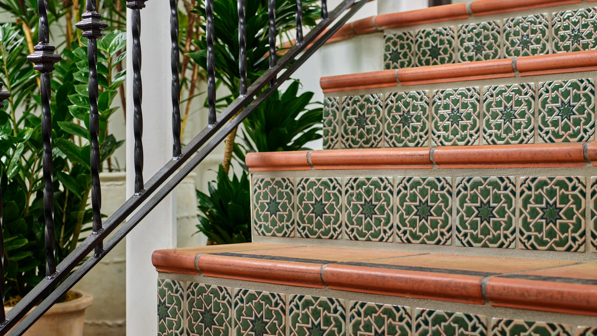 Staircase with dark green and red tiles with black metal railing near plants at Mar Monte Hotel in Santa Barbara, CA
