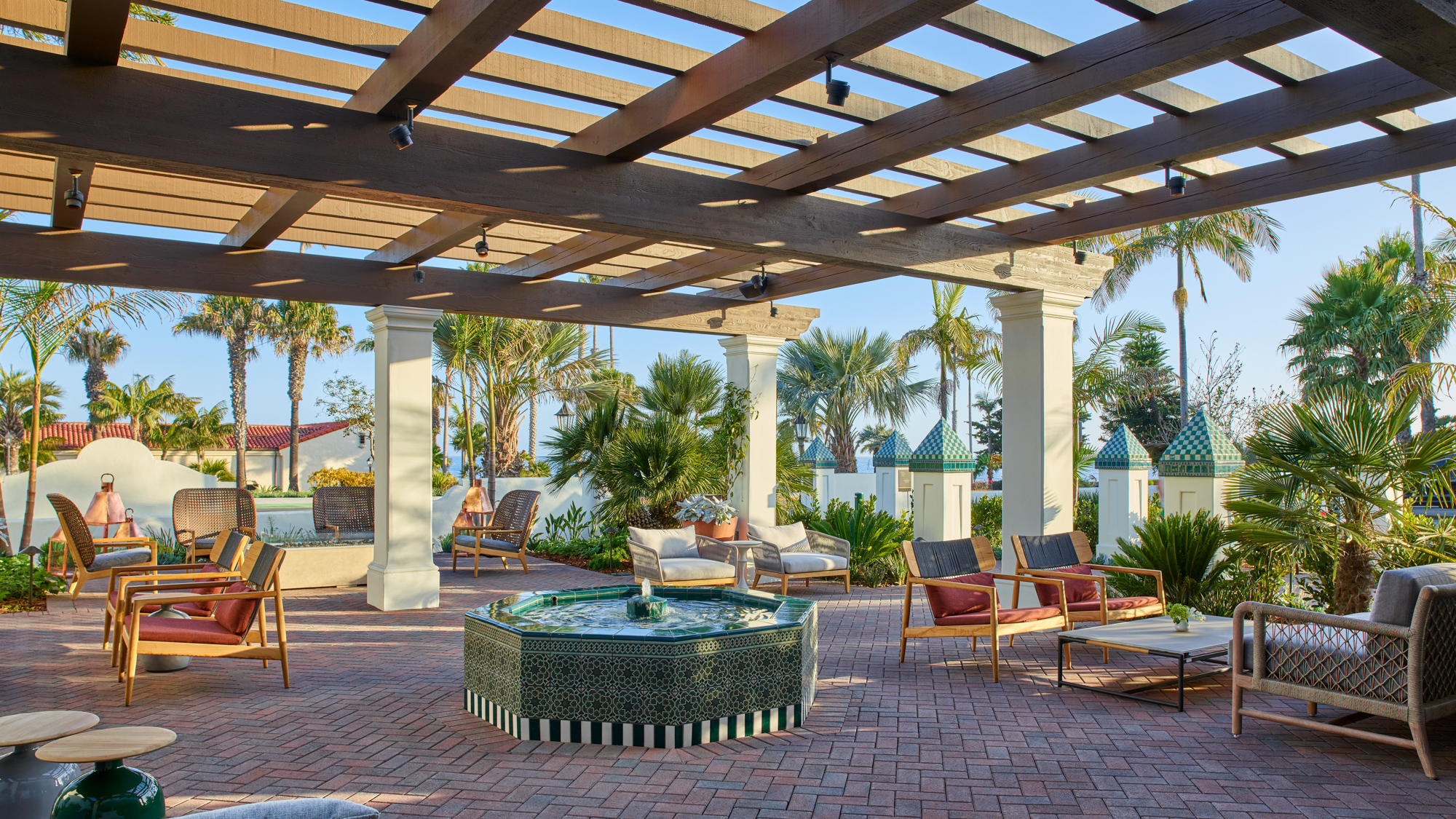 Outdoor patio area with grey lounge chairs and terrace roof above outdoor firepit near palm trees at Mar Monte Hotel in Santa Barbara, CA