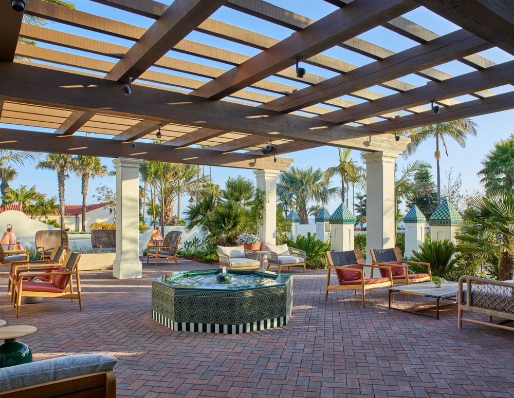 Outdoor patio area with lounge chairs and terrace roof above outdoor firepit near palm trees at Mar Monte Hotel in Santa Barbara, CA