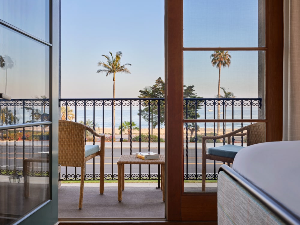 Patio and patio furniture overlooking roadway, ocean and white sand beach with palm trees at Mar Monte Hotel in Santa Barbara, CA