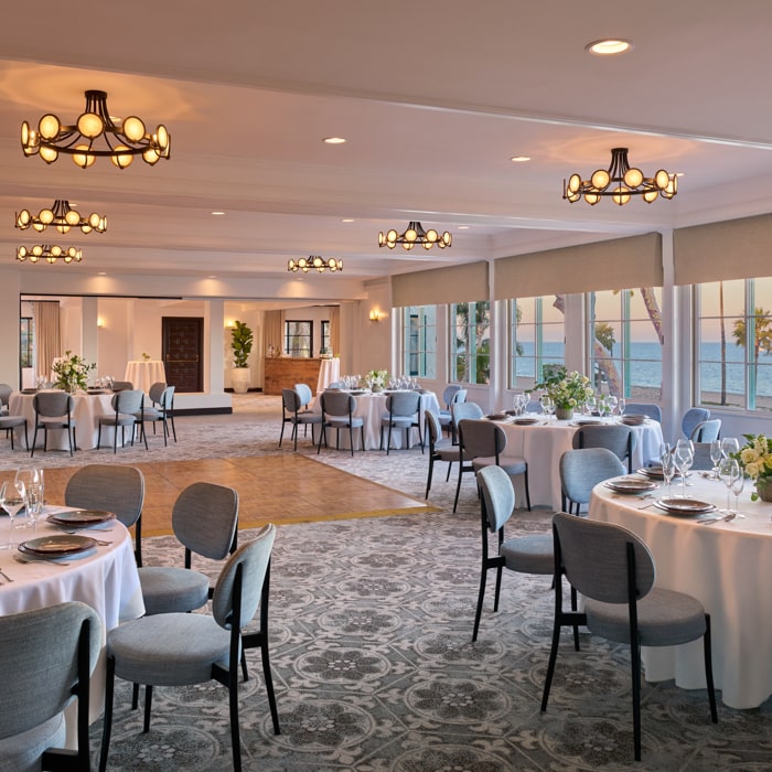 Event room with blue chairs and round tables adorned with white linens, silverware and glassware as well as flower centerpieces at Mar Monte Hotel in Santa Barbara, CA