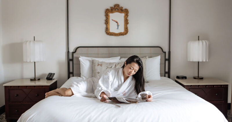 Woman wearing a robe and laying on bed while reading a magazine