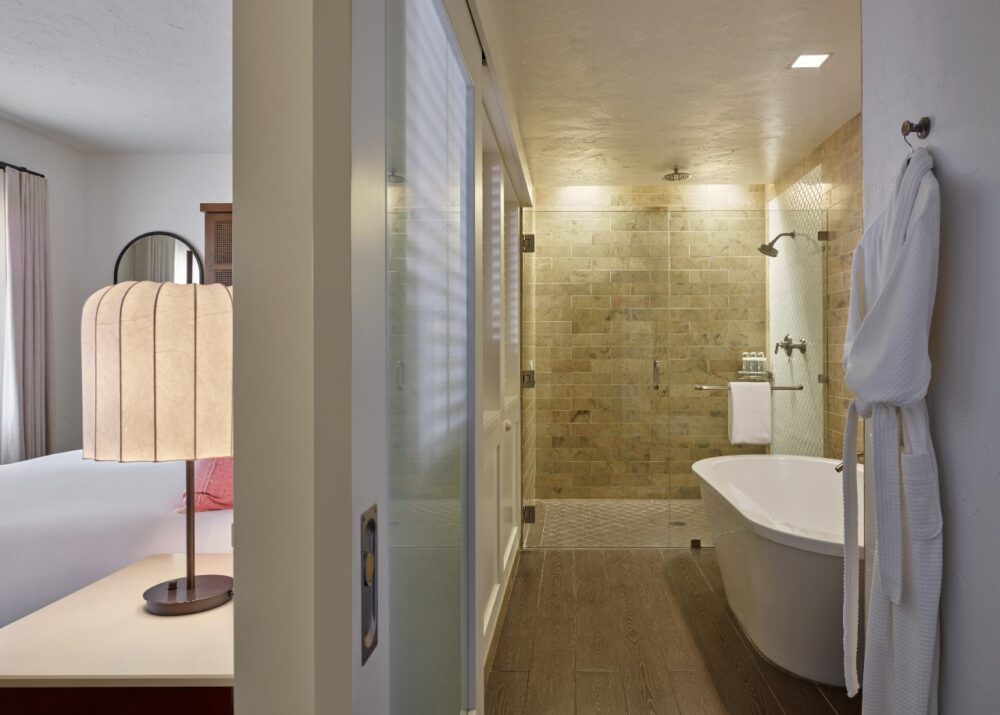 A bathroom with a large walk-in shower and a freestanding tub, with a white robe hanging on the wall.