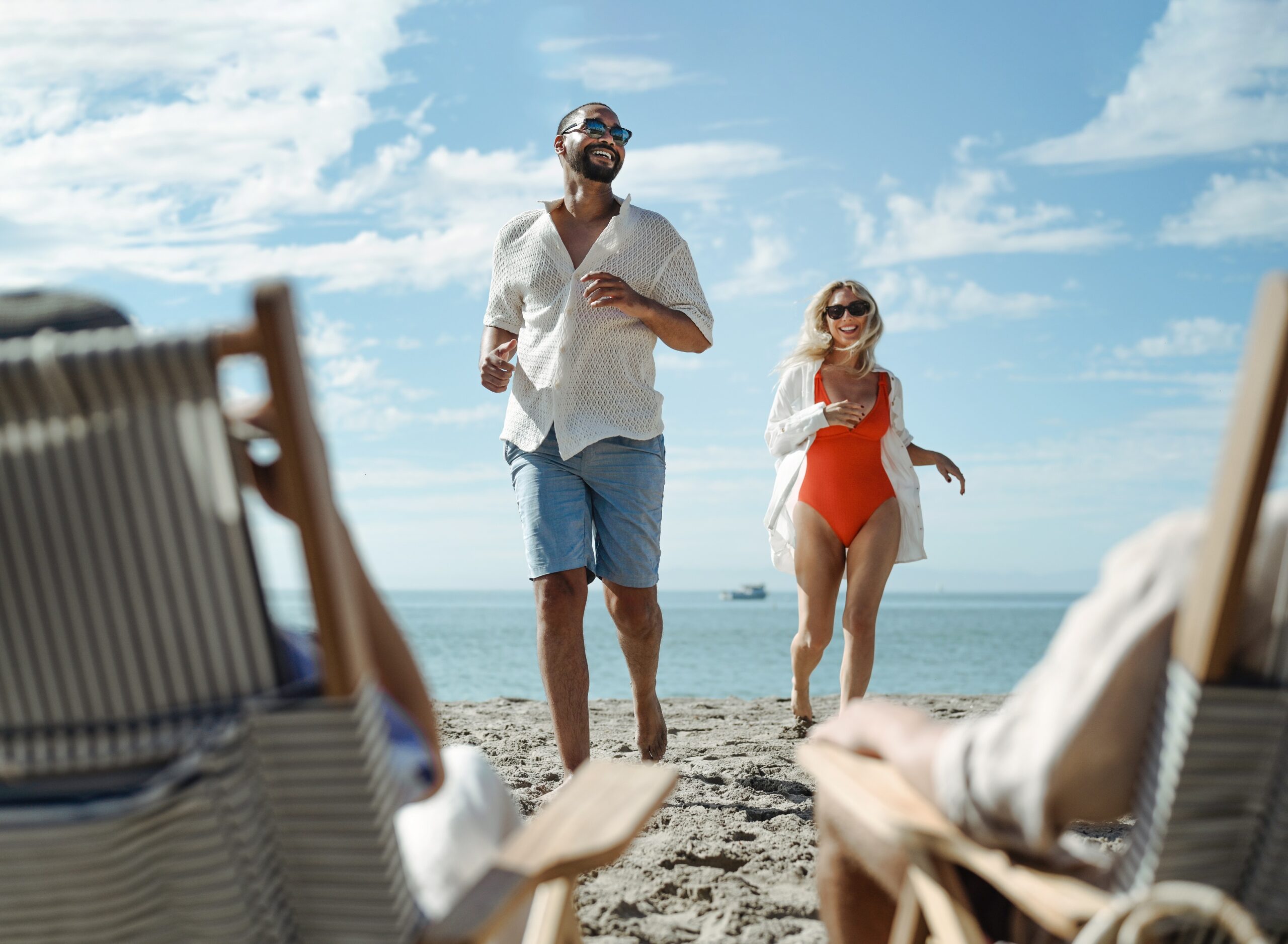 Guy and girl running on beach wearing swimsuits and sunglasses
