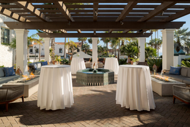 An outdoor space with a pergola, fire pit, and white tables.