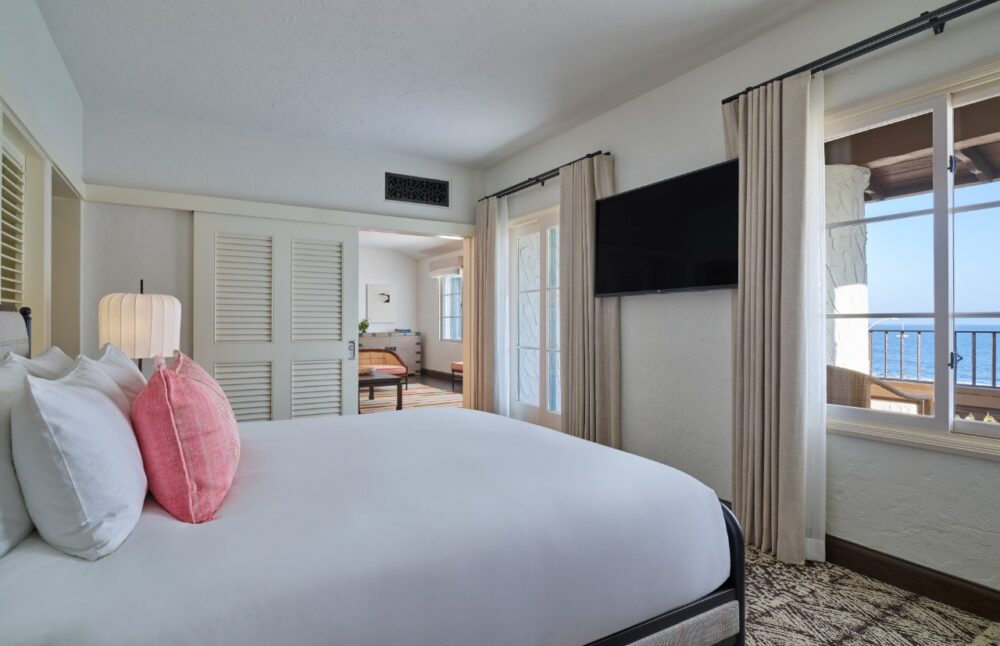 A wide view of a hotel room with a large bed, flat-screen TV, and ocean view.
